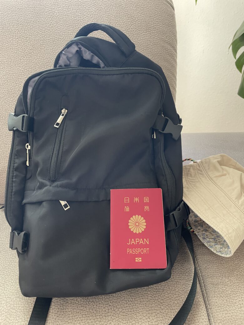 旅準備に使う黒いバックパックと日本のパスポート、白い帽子