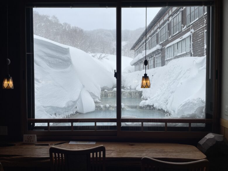 酸ヶ湯温泉旅館では温泉の川が流れる豪雪景色をみながら共用スペースではテレビを見たりPCで仕事をしたりしている方も。